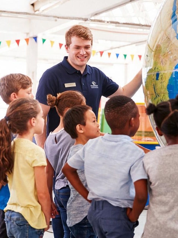 Science center educator showing a large globe to a group of children